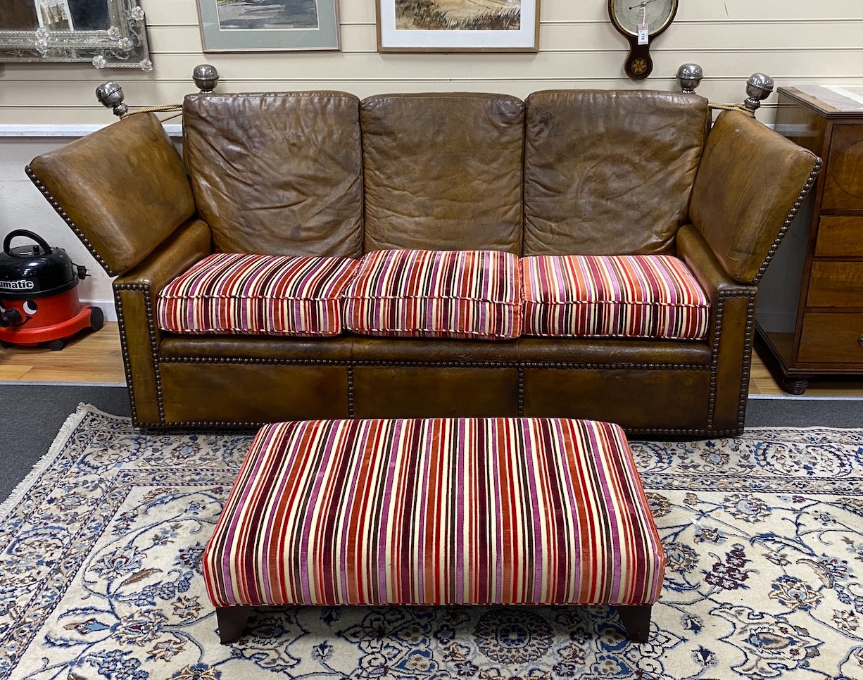 A studded tan leather Knowle settee with striped fabric loose cushion seat, length 220cm, depth 96cm, height 110cm and matching footstool, width 104cm, depth 64cm